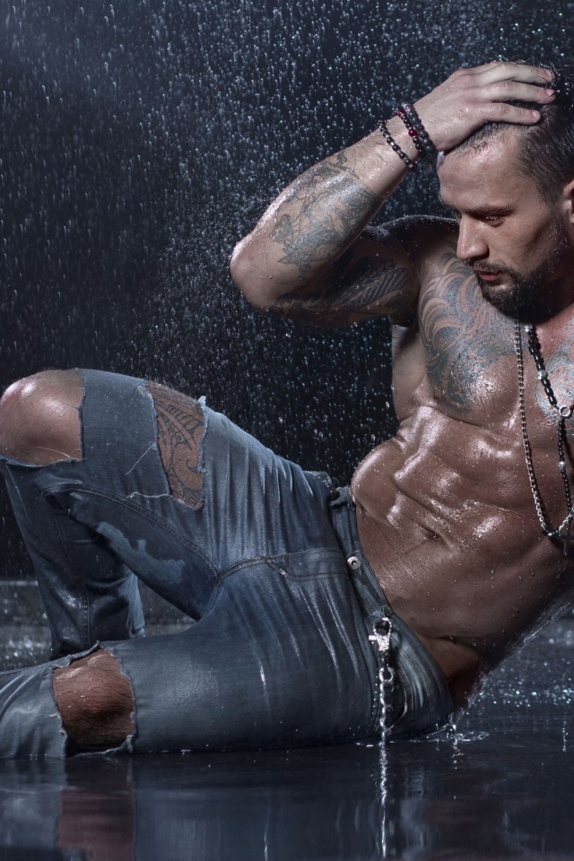 Мужчина в татуировках лежит на земле под дождем