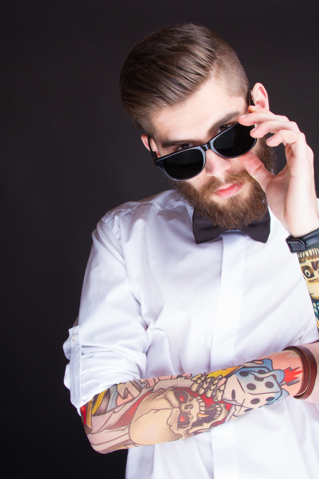 Мужчина в очках с татуировками на руках на сером фоне