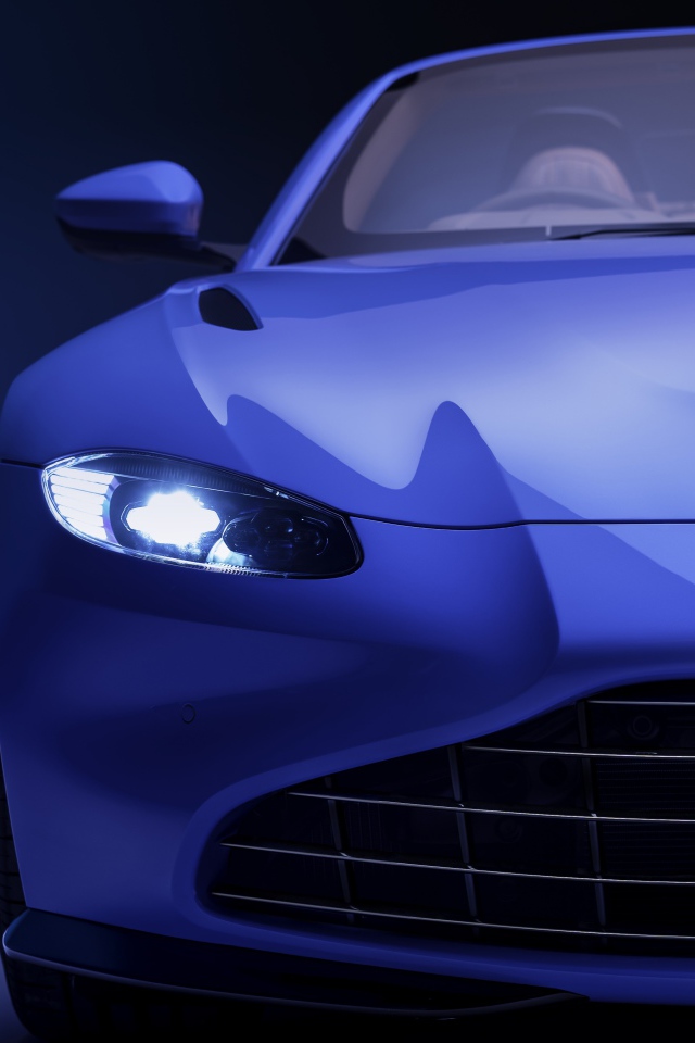 Синий автомобиль Aston Martin Vantage Roadster 2020 года с включенной фарой 
