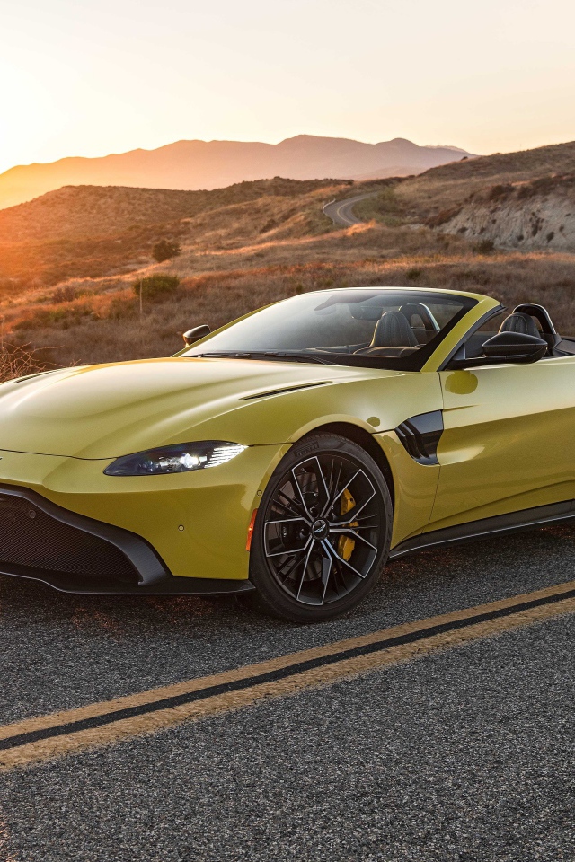 Желтый кабриолет  Aston Martin Vantage Roadster, 2021 года на трассе на рассвете