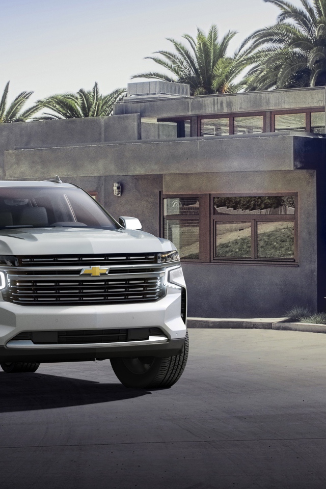 Серый внедорожник Chevrolet Suburban, 2021 года на фоне дома