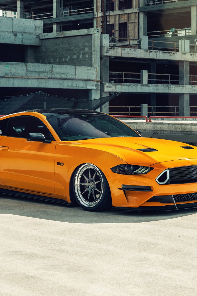 Оранжевый автомобиль Mustang у заброшенного здания 