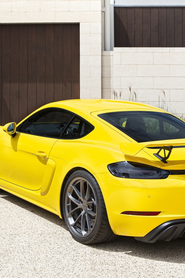 Желтый автомобиль Porsche 718 Cayman GT4, 2020 года у гаража 
