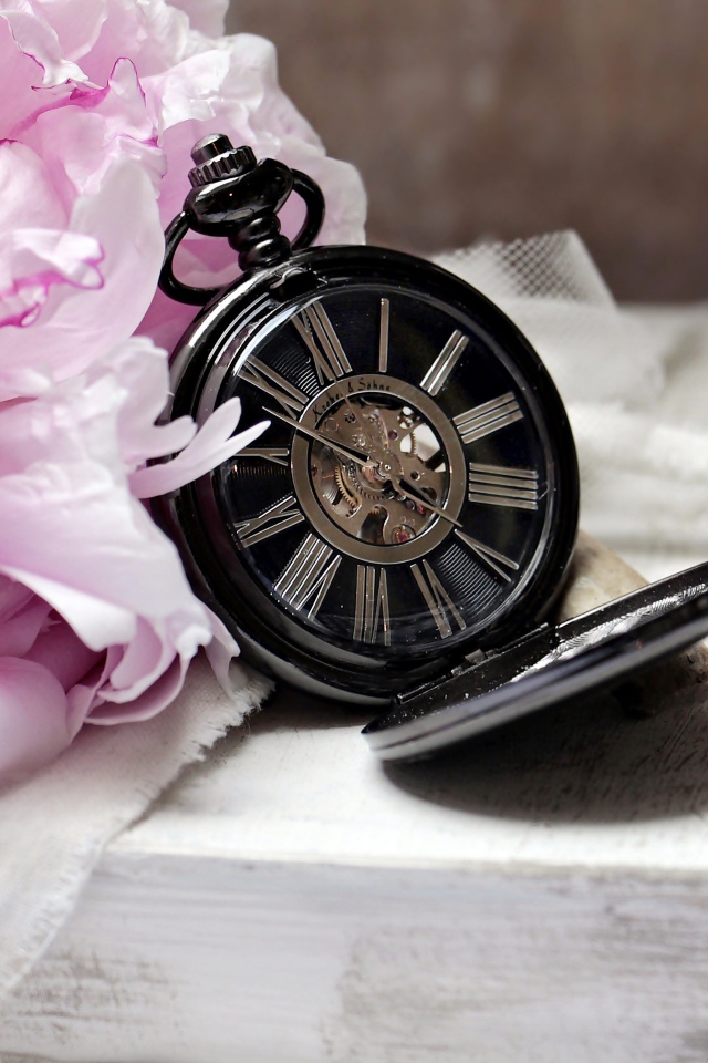 Черные карманные часы с книгой и цветами на столе 