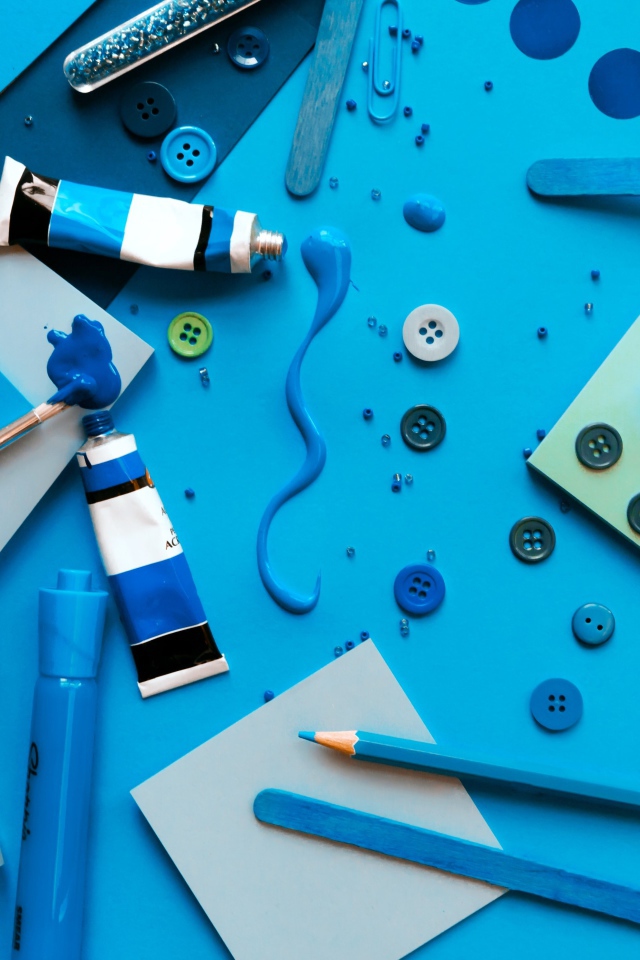 Синие краски и канцелярские предметы на столе с бумагой 
