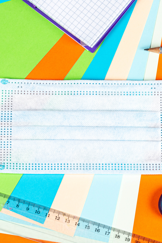 Маска от коронавируса лежит на цветной бумаге с канцелярскими предметами