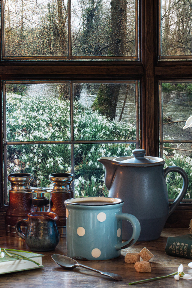 Керосиновая лампа на столе с кружкой, книгами и букетом подснежников у окна