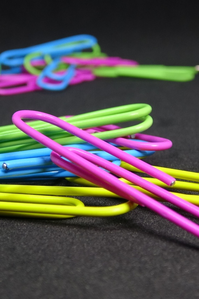 Разноцветные скрепки на черном столе 