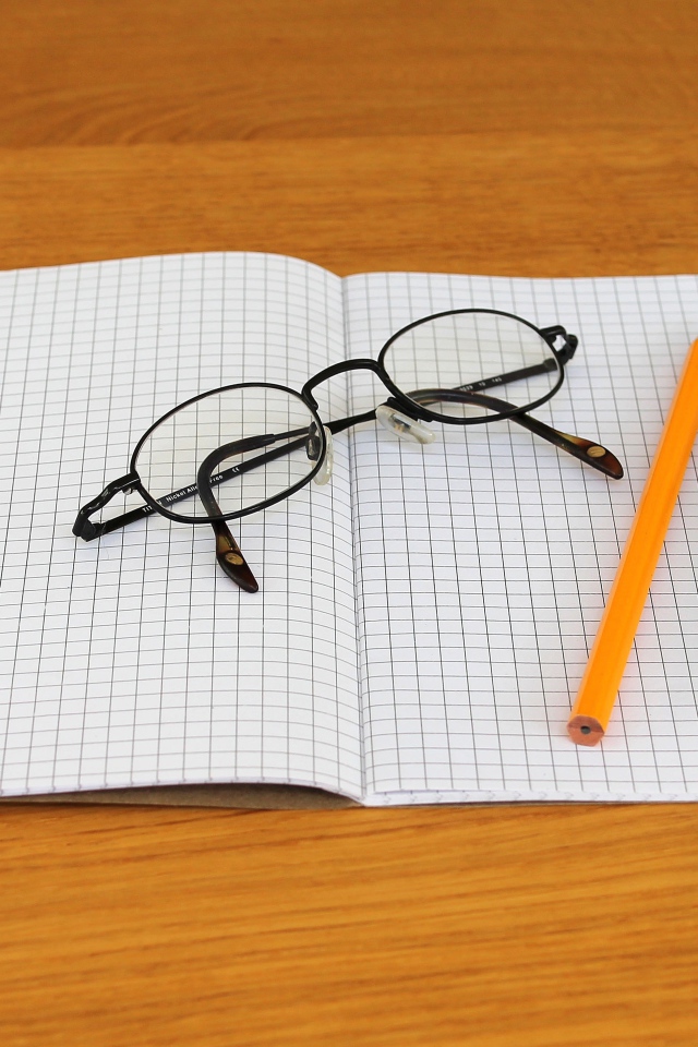 Тетрадь, ручка, карандаш и очки лежат на парте