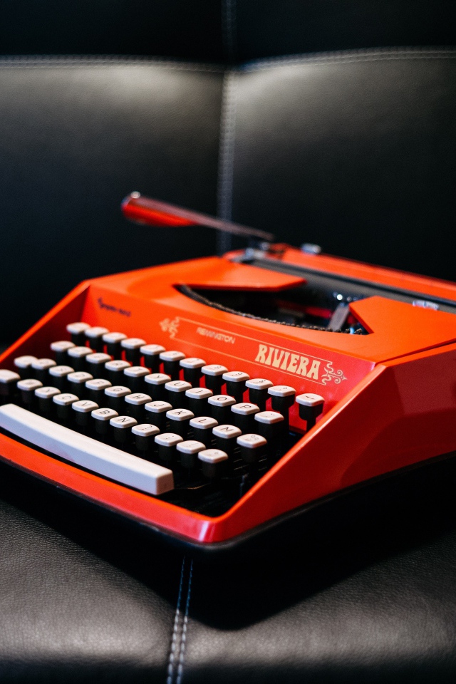 Старая красная печатная машинка на черном диване