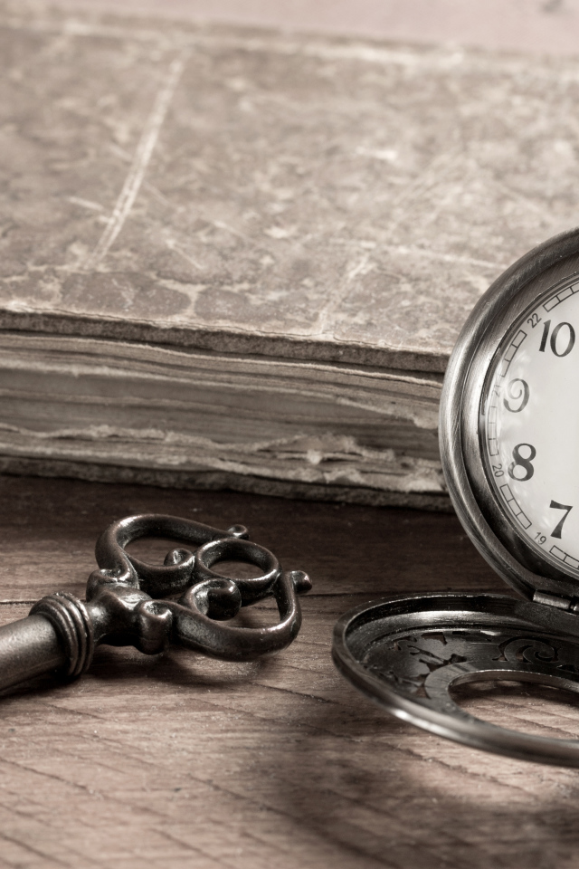 Pocket watch on a table with a key and an old book