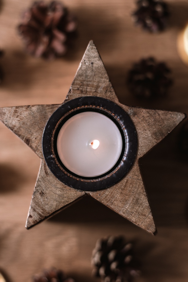 Свеча в форме звезды на столе с шишками и сушеным апельсином