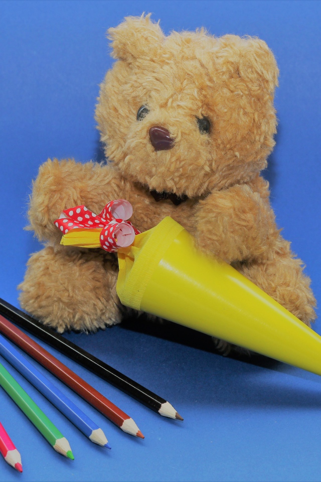 Игрушечный медвежонок  с карандашами на синем фоне