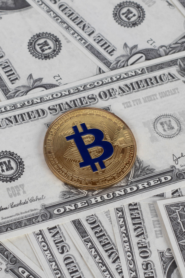 Bitcoin coin lies on hundred dollar bills
