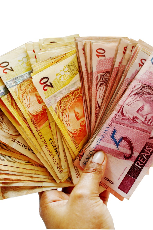 Много купюр бразильского реала в руке на белом фоне 