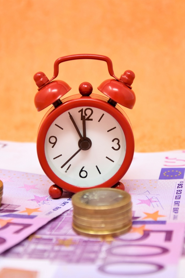 Маленький красный будильник с купюрами евро и монетами