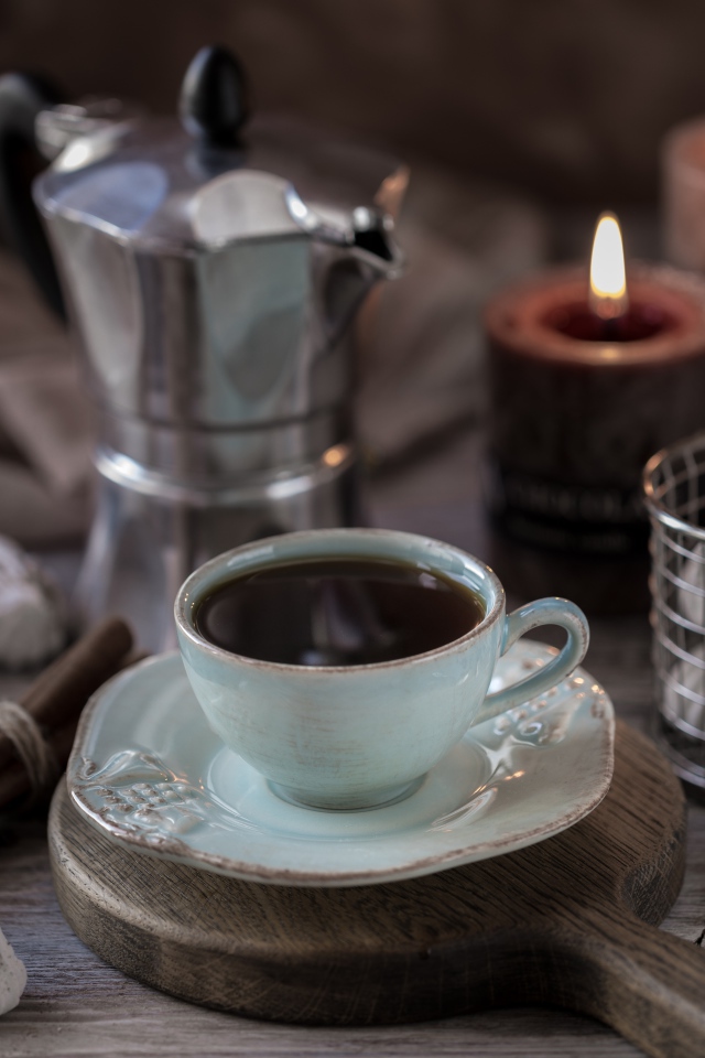 Чашка эспрессо на столе с корицей, зефиром и зажженными свечами