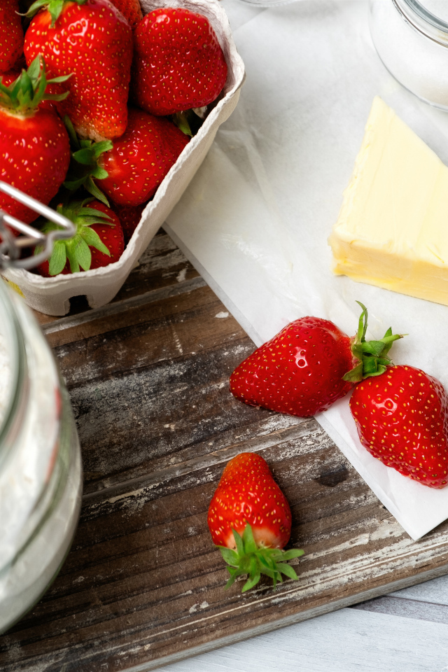 Кусок масла на столе с клубникой и мукой 