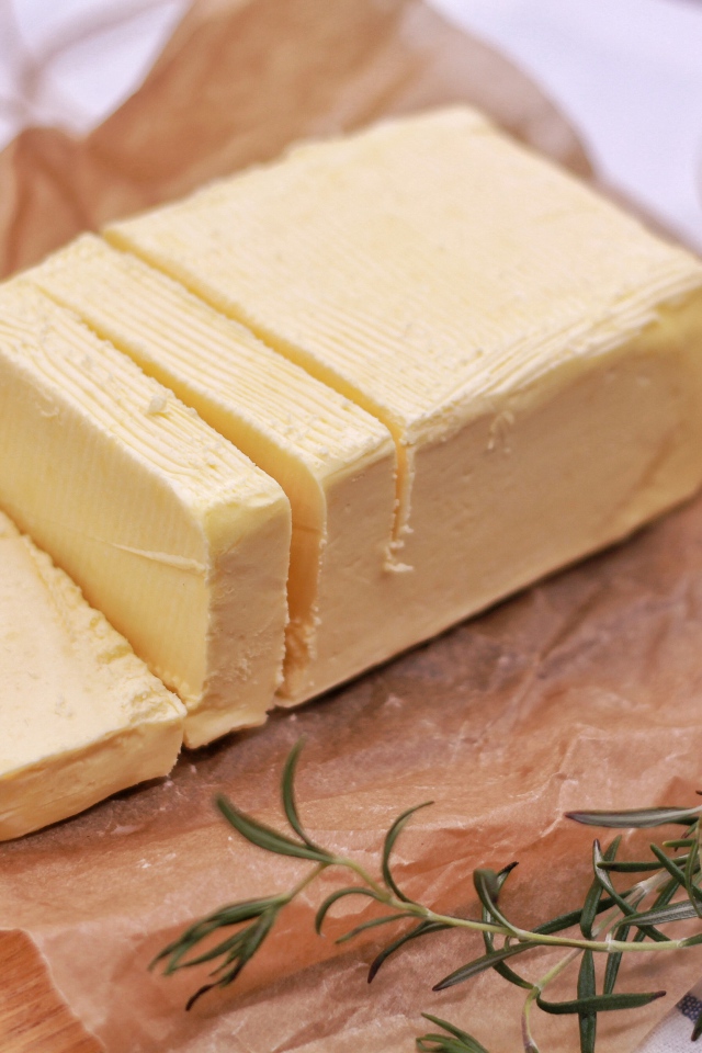 Кусок свежего сливочного масла на столе с розмарином и чесноком