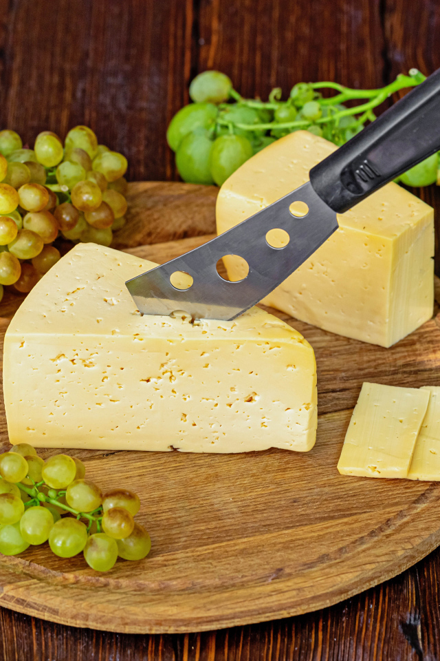 Кусок твердого сыра на столе с ножом и белым виноградом