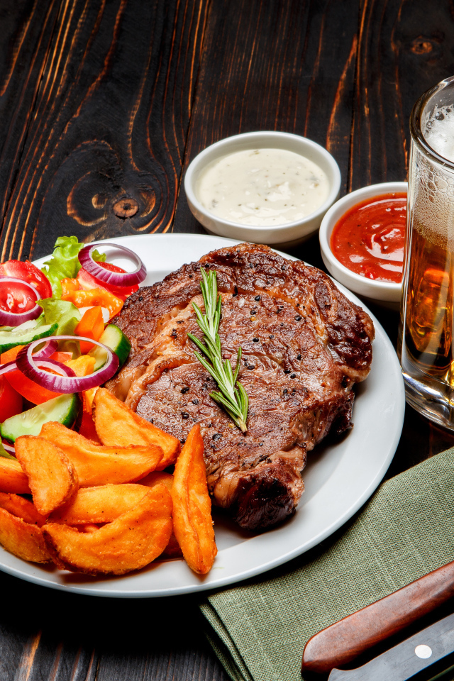 Кусок мяса на тарелке с картофелем и салатом на столе с соусом и пивом