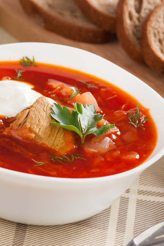 Тарелка горячего борща на столе с хлебом и чесноком