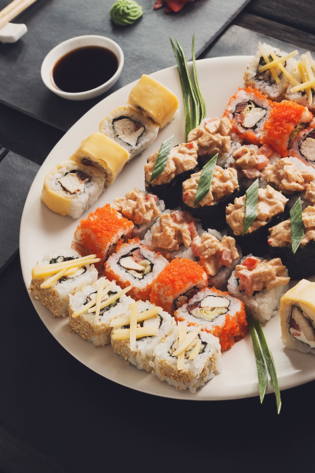 Аппетитные роллы на большой тарелке на столе с соусом