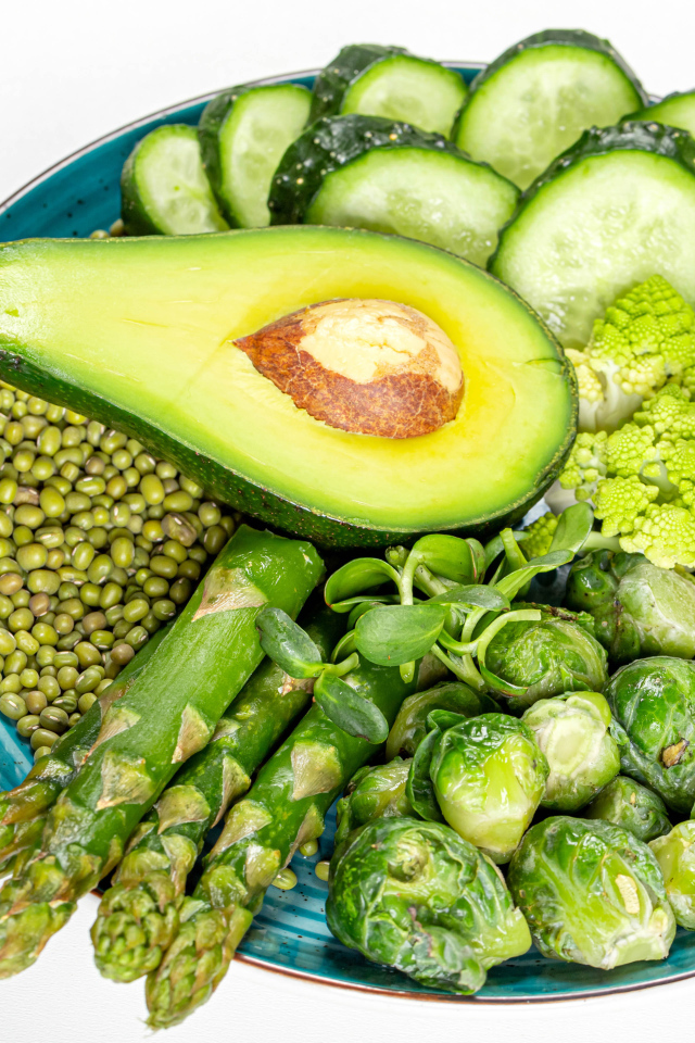 Авокадо, капуста, огурцы и спаржа на тарелке на белом фоне