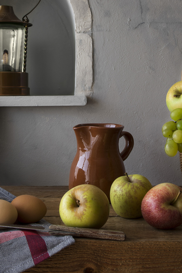 Корзина с яблоками и виноградом на столе с хлебом и яйцами