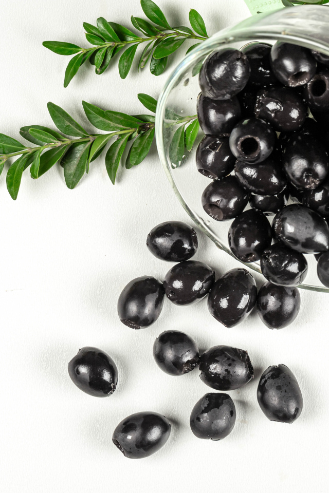 Черные маслины с розмарином на белом фоне