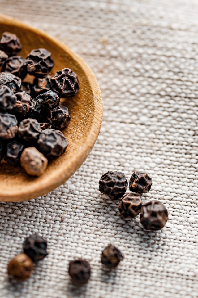 Черный перец горошком на деревянной ложке