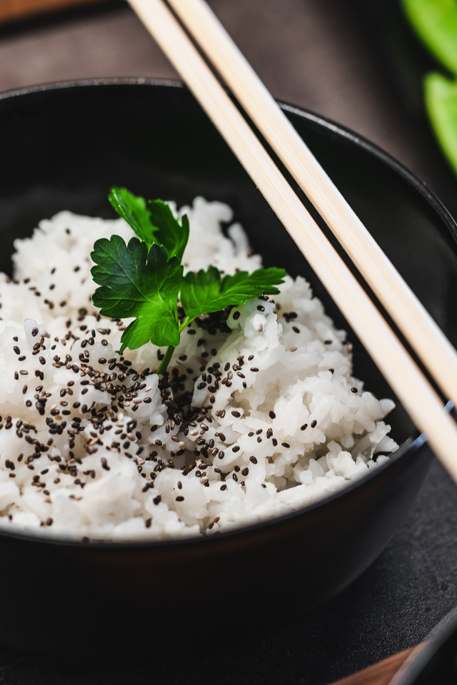 Вареный рис с семенами  в черной миске с палочками