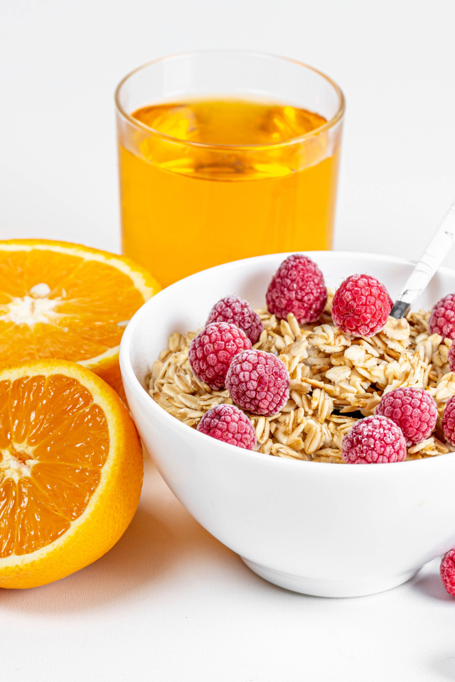 Миска мюсли с ягодами малины и апельсинами на столе с соком