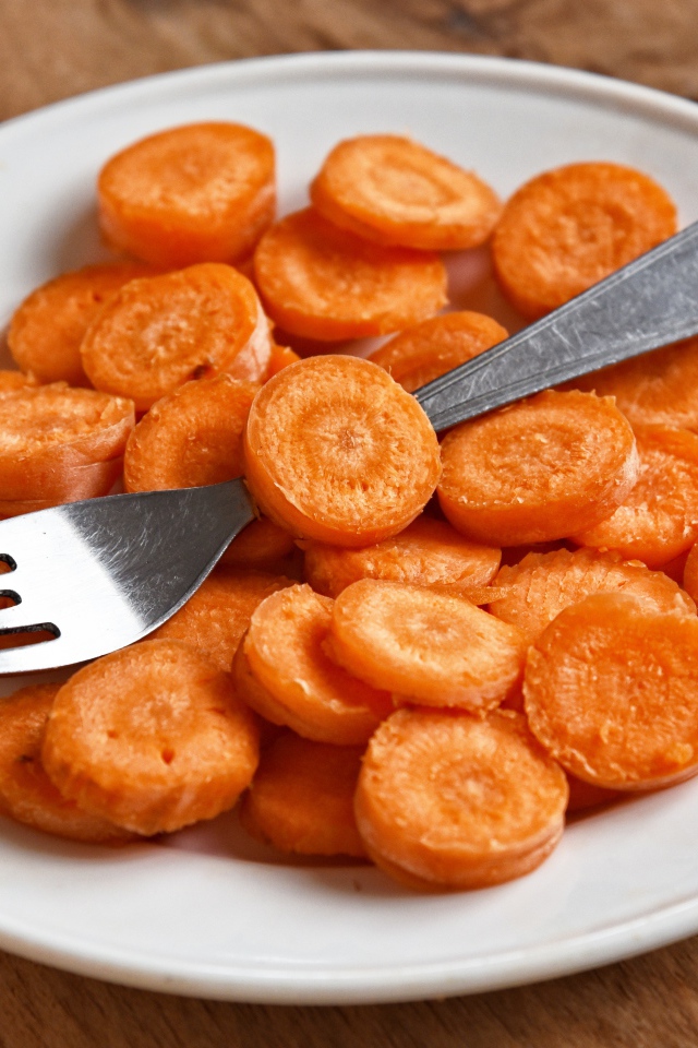 Морковь кружочками на белой тарелке с вилкой