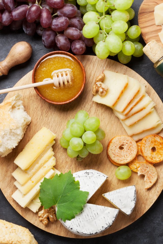 Сыр на столе с виноградом, оливками и белым вином