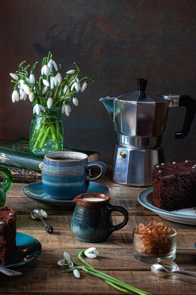 Шоколадный торт на столе с кофе, букетом подснежников и лампой