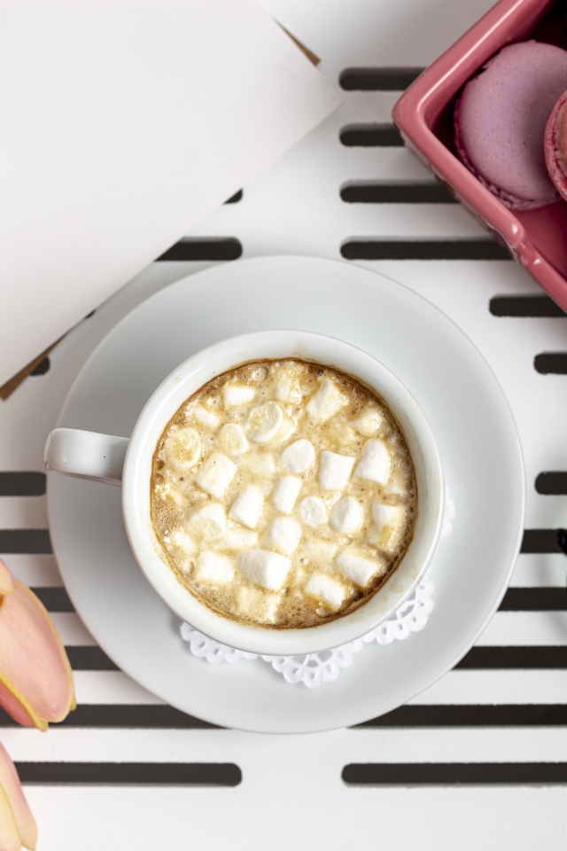 Чашка какао с маршмеллоу на столе с букетом тюльпанов, десертом макарун и очками