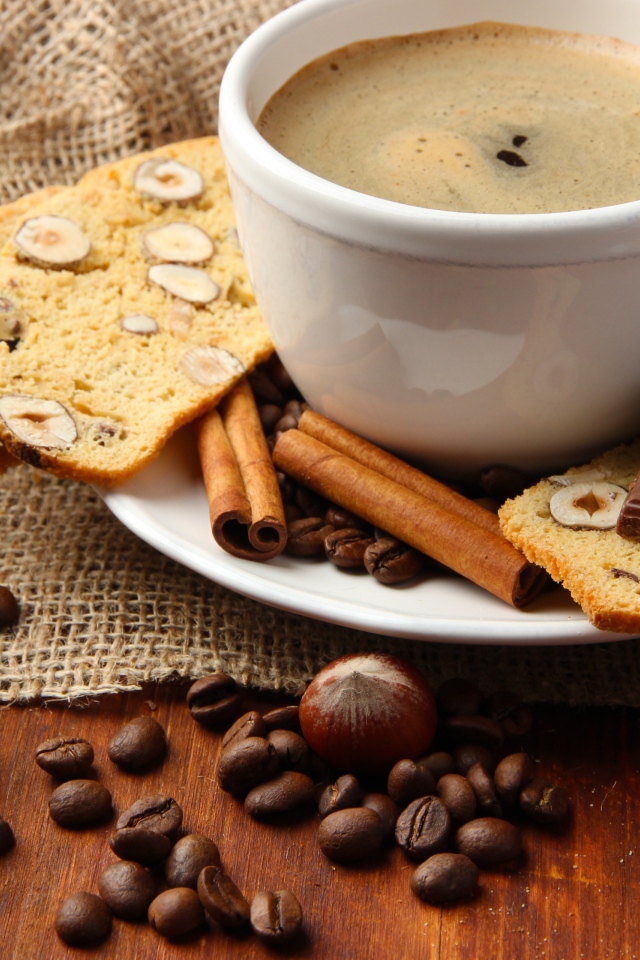 Чашка кофе на тарелке с кексом, шоколадом, корицей и зернами 