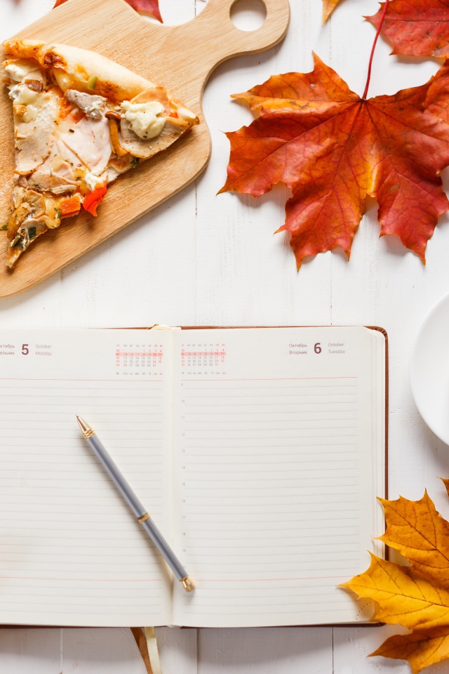 Ежедневник на столе с желтыми листьями, кофе и пиццей 