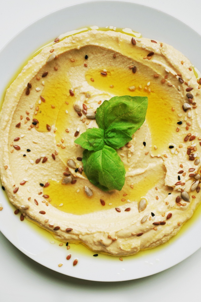 Блюдо хумус размазан по тарелке на сером фоне