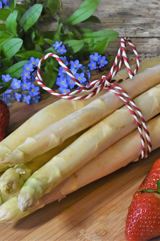 Свежая спаржа на столе с клубникой и цветами незабудками