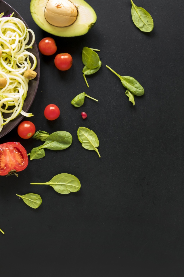 Салат из свежих овощей на черном столе с базиликом, помидорами и авокадо 