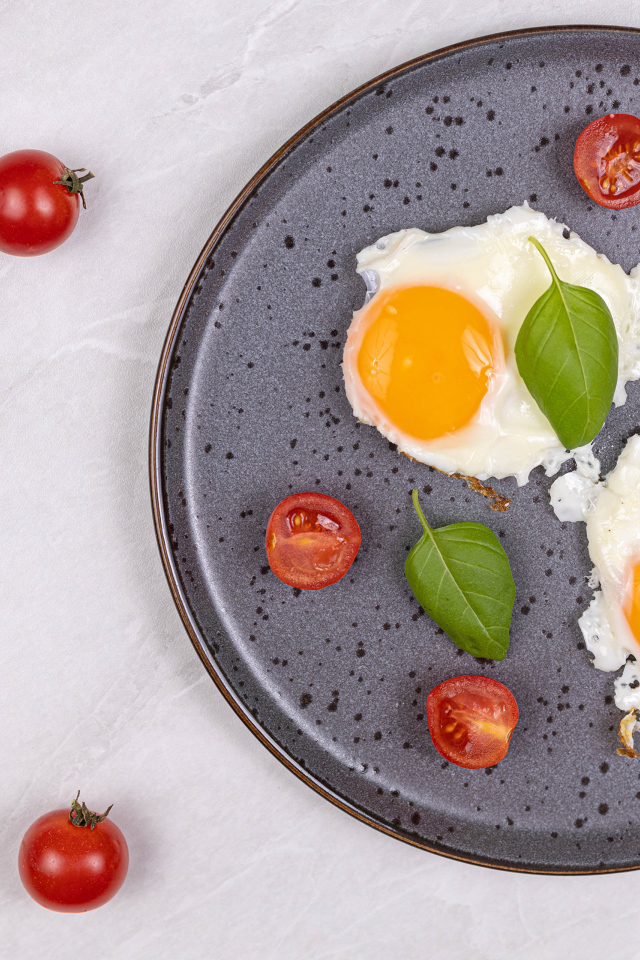 Яичница глазунья с помидорами и листьями базилика на черной тарелке 