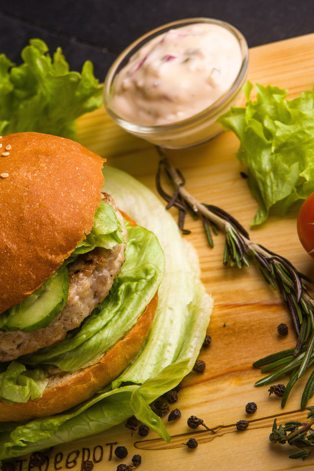 Гамбургер на столе с листьями салата, специями, помидорами и соусом