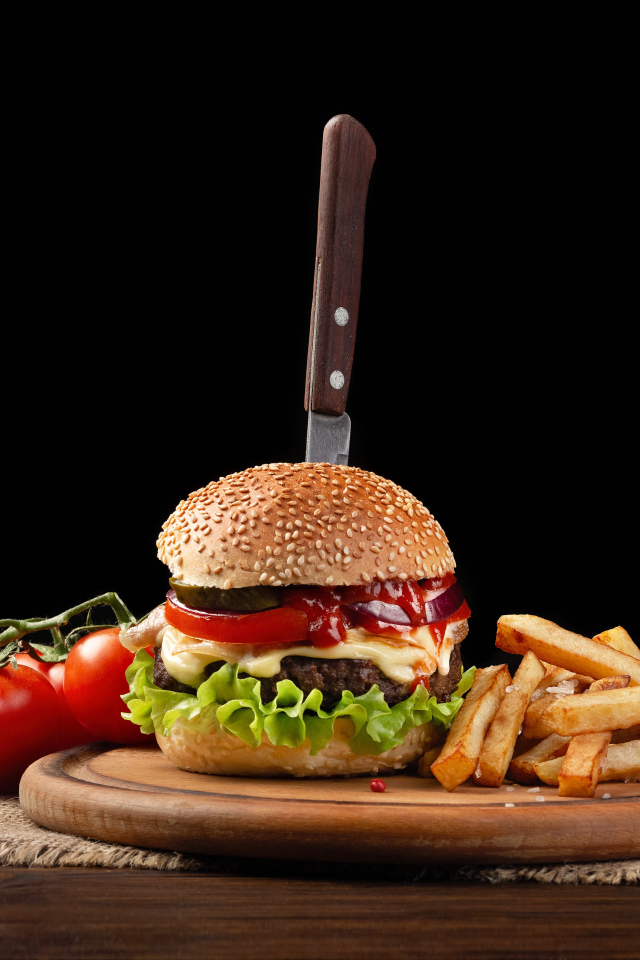 Гамбургер с ножом на столе с помидорами и картофелем фри 