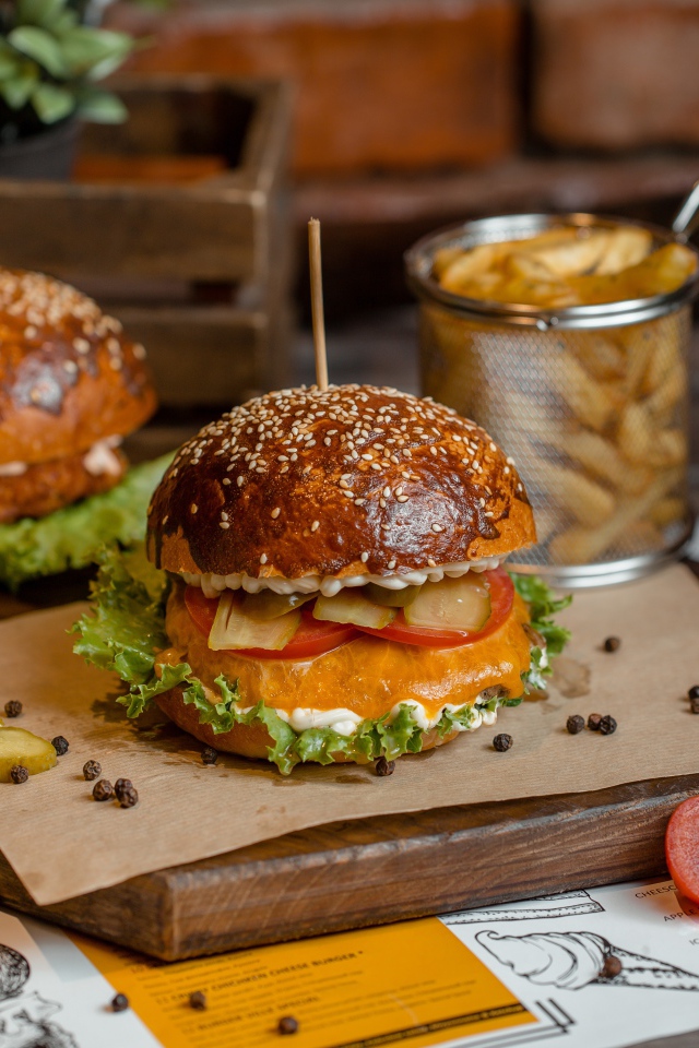 Гамбургеры на столе с помидорами, картофелем фри и солеными огурцами