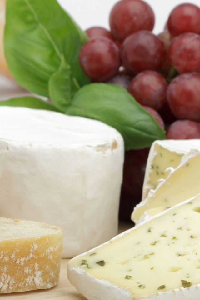 Твердый сыр на столе с батоном и виноградом