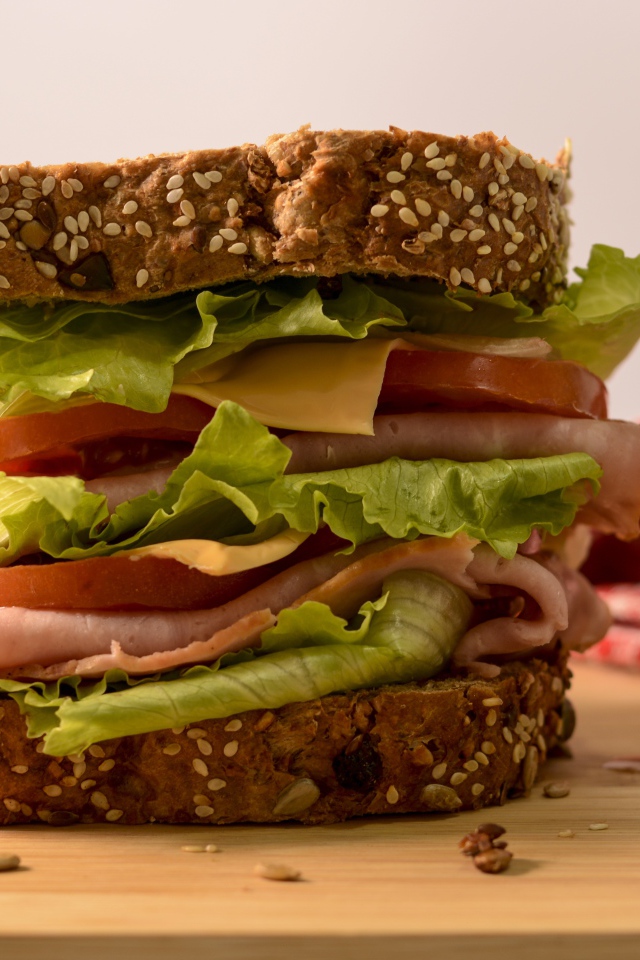 Большой бутерброд с ветчиной, сыром, помидорами и листьями салата 