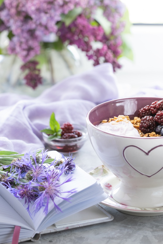 Мюсли с ягодами в чашке на столе с блокнотом и букетом сирени 