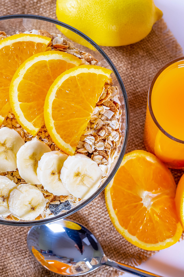 Овсяные хлопья в тарелке с кусочками банана и апельсина на столе с соком